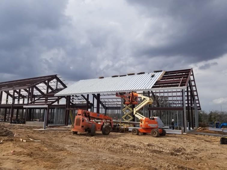 Crew erecting a pre-engineered steel building frame using two boom lifts on a cleared site