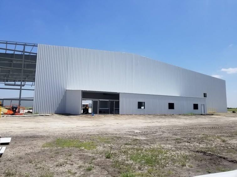 Finished grey and white metal industrial building with a raised parapet, glazed entry and a gravel lay-down area