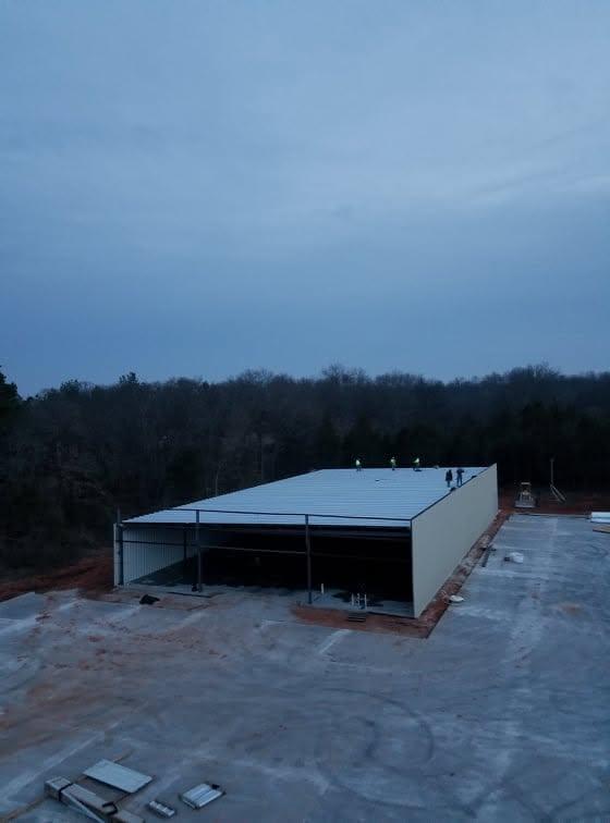 Completed metal hangar photographed at dusk against a deep blue sky, with the apron lighting just coming on