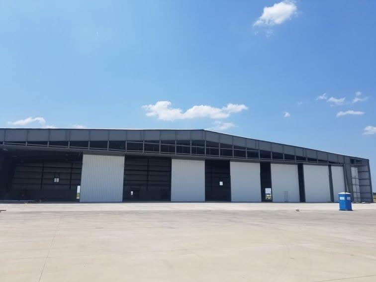 Completed airport hangar with four large bay doors and a standing seam roof, seen across the concrete apron