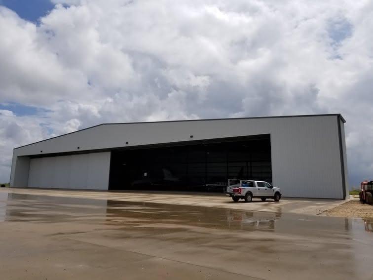 Metal aircraft hangar with one large bay door rolled open and a pickup truck parked on the wet apron outside