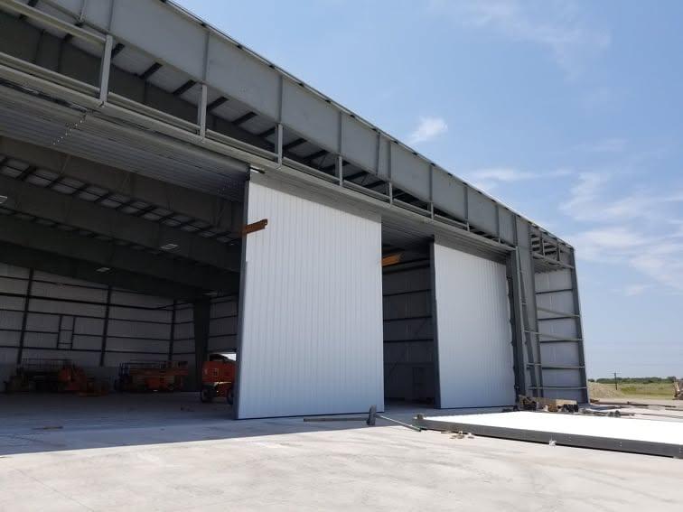 Aircraft hangar with large sliding doors partially open, showing the door track and framed opening