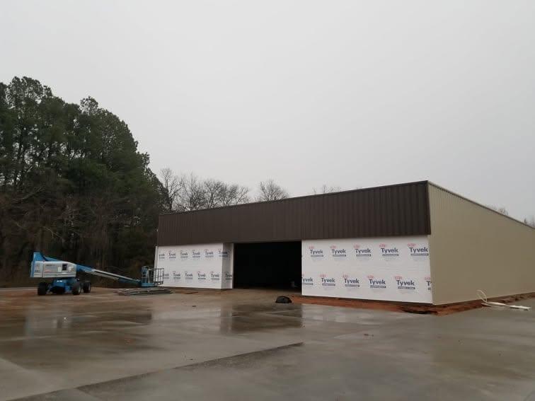 Tan metal building with a dark open bay opening and a boom lift parked alongside the finished wall panels