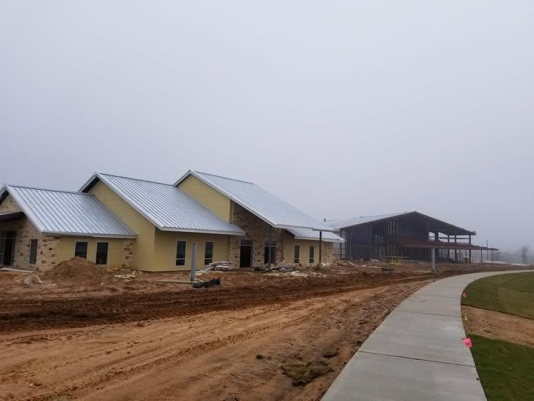 Multi-building lodge site under construction with several metal buildings and stone-clad facades along a new access road