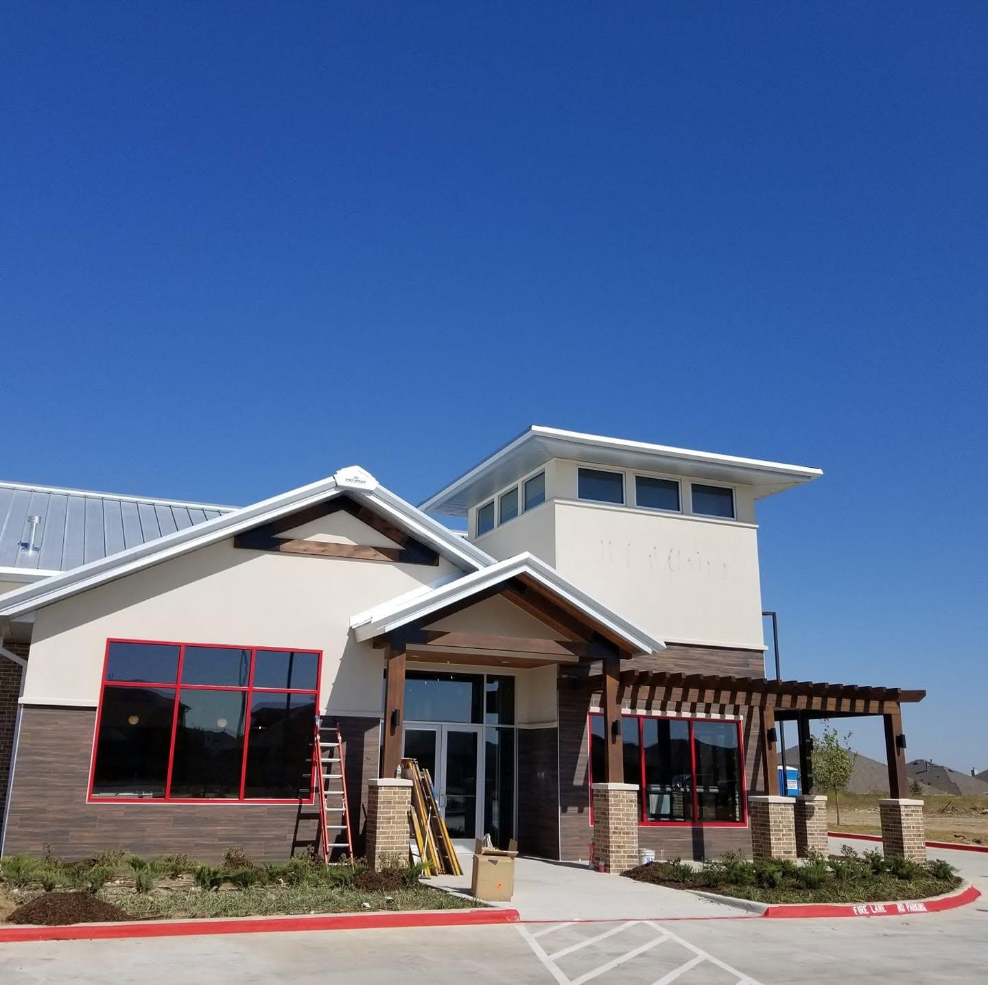 Finished two-storey commercial office and retail building with white stucco, red trim and a covered entry pergola