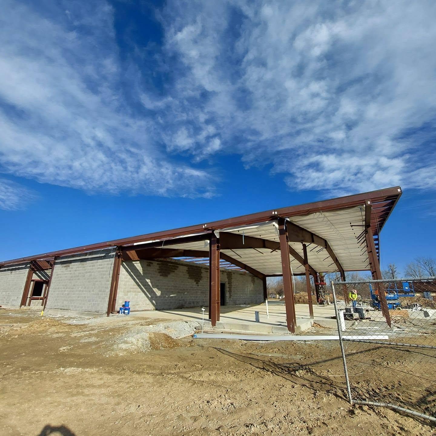 Open-air steel pavilion structure with curved rafters and a partially installed metal roof
