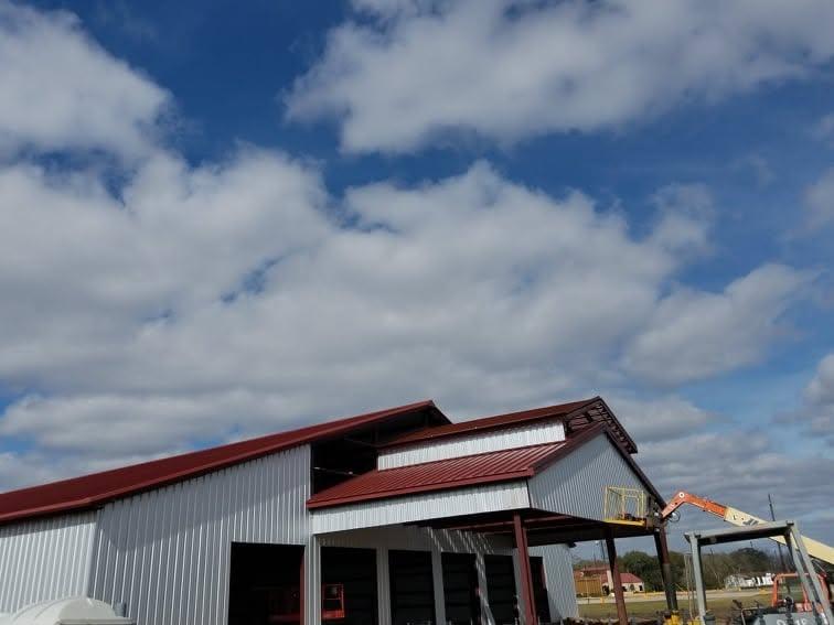 Commercial metal building with red trim and grey siding partly installed, boom lift working the upper wall
