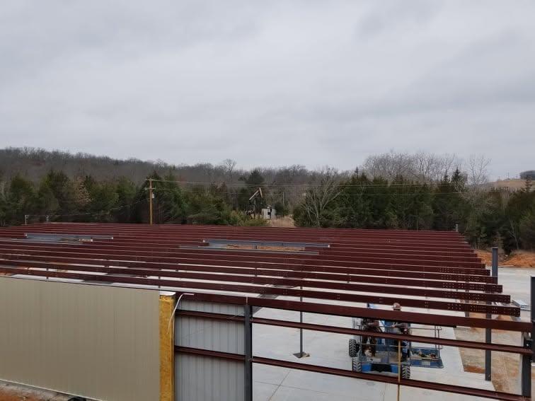 Red primed steel frame with roof purlins installed and light grey wall panels going up on the end wall