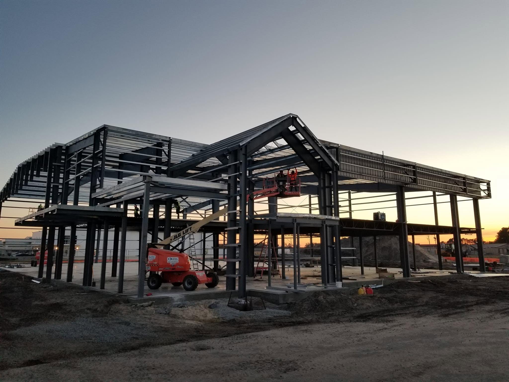 Steel building frame standing against a sunset, with a boom lift and crew working at height